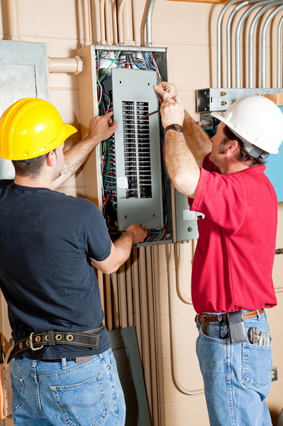 two electricians working on large electrical panel