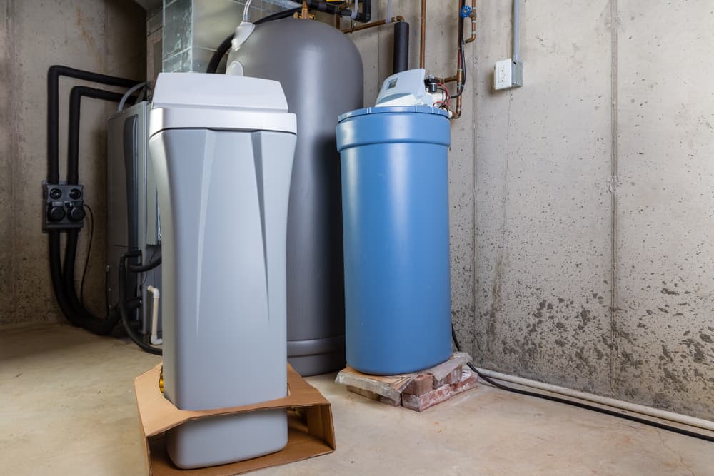 Old and new water softener tanks in a utility room waiting for replacement to remove minerals from hard water